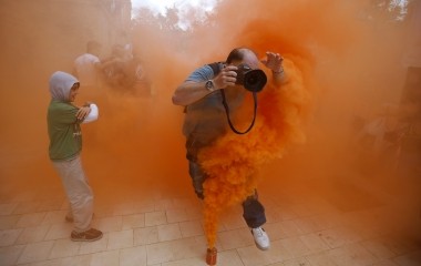 A photographer jumps over a smoke canister during a demonstration by firefighters, security and military personnel against cuts in their salaries imposed by Spanish Government, in the Andalusian capital of Seville
