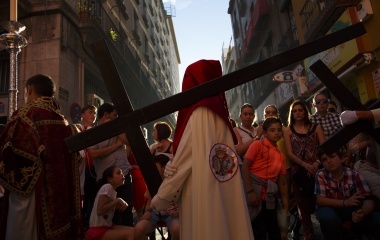 Penitent of La Lanzada brotherhood carries a cross next to people who gather to see the procession during Holy Week in the Andalusian capital of Seville