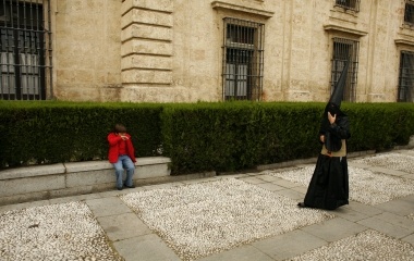 Penitent of 'Los Estudiantes' brotherhood walks as a boy sits on a bench during Holy Week in the Andalusian capital of Seville