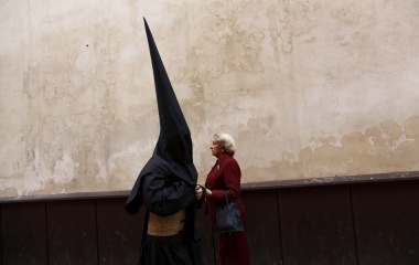 A penitent walks past a woman on his way to a church before taking part in the procession of "La Borriquita" brotherhood during the Palm Sunday in the Andalusian capital of Seville