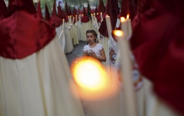 A girl holds a ball of wax between penitents of La Lanzada brotherhood during Holy Week in the Andalusian capital of Seville