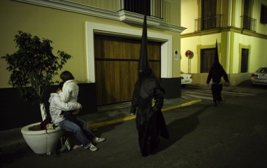A couple embrace each other as penitents walk to a church before taking part in the procession of "El Gran Poder" brotherhood during Holy Week in Seville