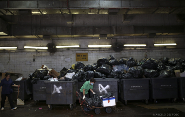 A woman unloads garbage bags from a wheelbarrow in a dumpster in the Central district in Hong Kong