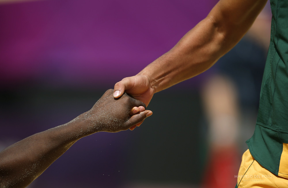 South Africa's Grant Goldschmidt helps his team mate Freedom Chiya to stand up during their men's preliminary round beach volleyball match against Latvia at the London 2012 Olympic Games at Horse Guards Parade